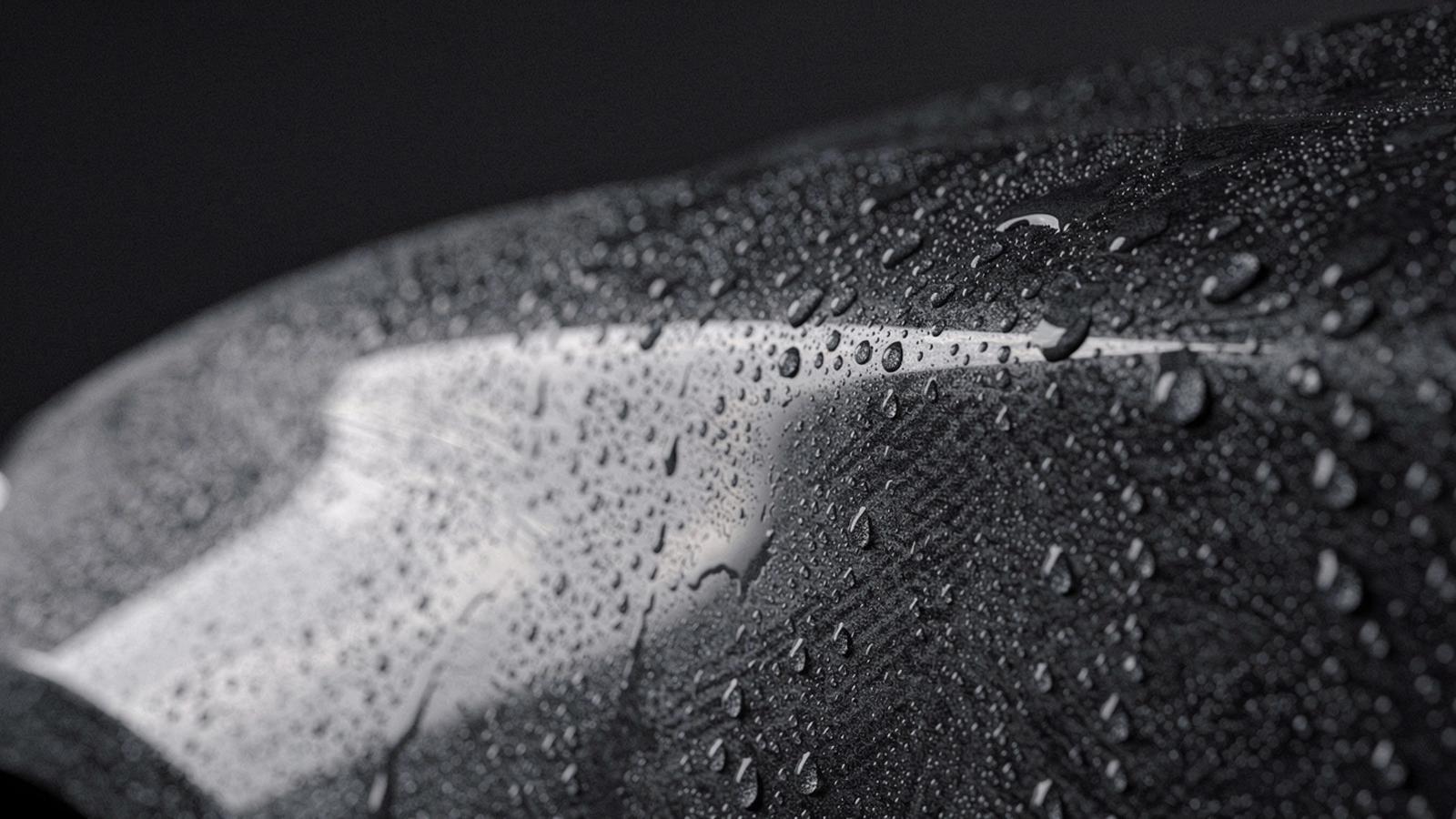 Macro view of a dark car panel with water beading across the clear coat